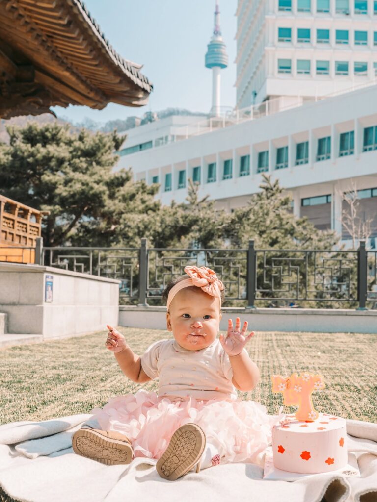 Baby girl sitting outdoors beside her first birthday decorations in Seoul