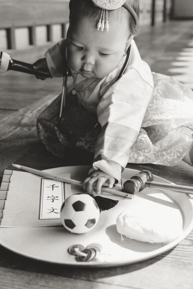 Black and white photo of a baby reaching for items during a traditional Korean first birthday celebration