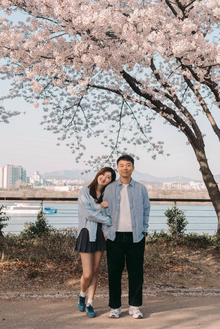 Couple posing beneath cherry blossoms beside the Han River in Seoul