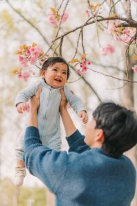 Parent lifting a smiling baby beneath spring blossoms during a Seoul kids photoshoot