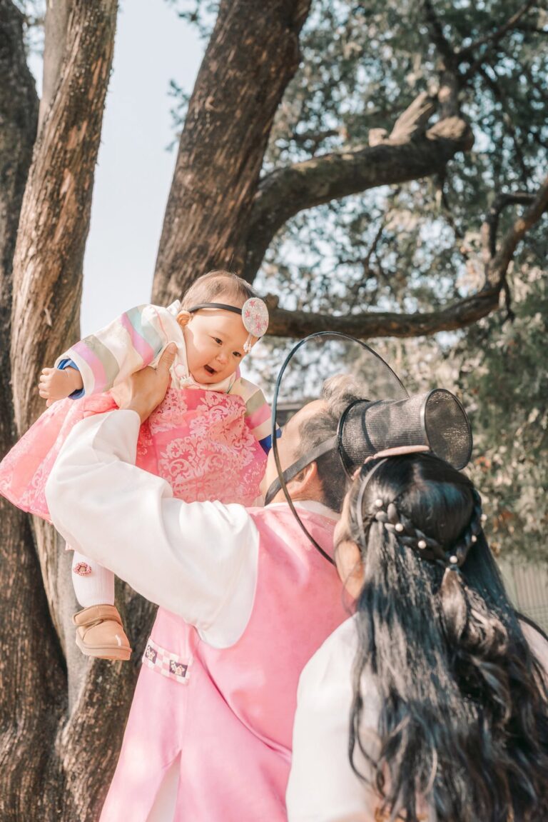 Parent lifting a laughing baby dressed in a pink hanbok during a Seoul photoshoot