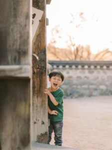 Young boy peeking playfully from behind a wooden post during a Seoul kids photoshoot
