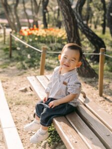 Young boy smiling while sitting on a wooden bench during an outdoor Seoul photoshoot