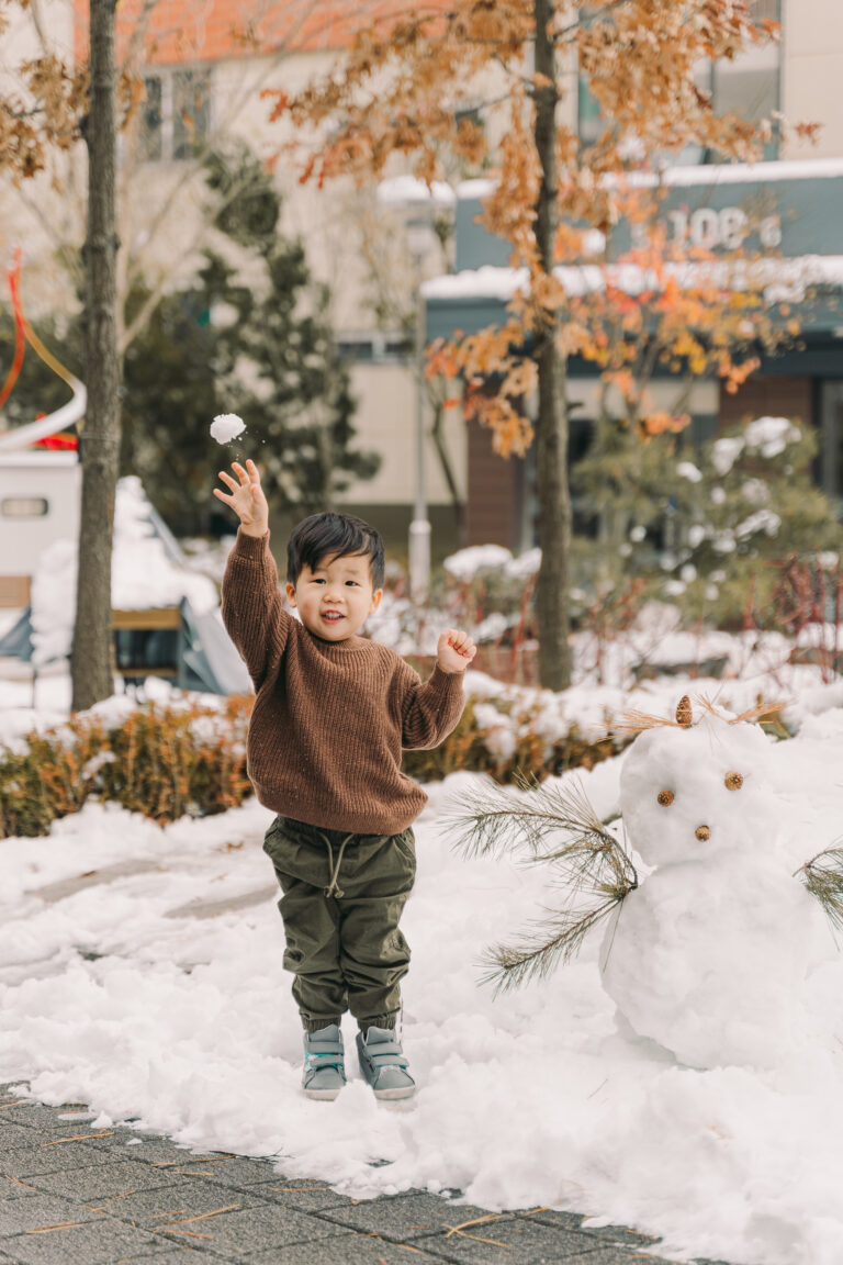 Young child playing outdoors in the snow during a winter photoshoot in Seoul