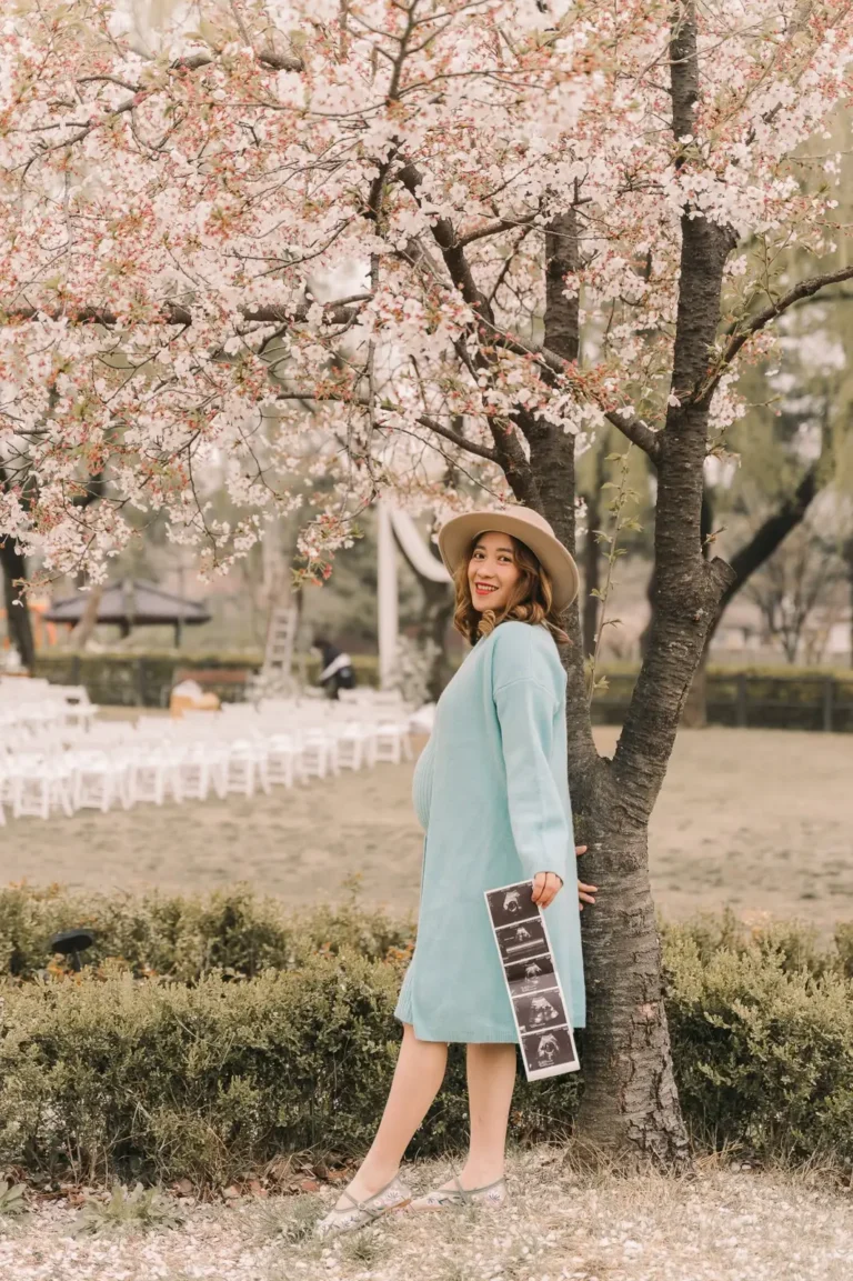 Pregnant woman in a blue dress posing beneath cherry blossoms in Seoul