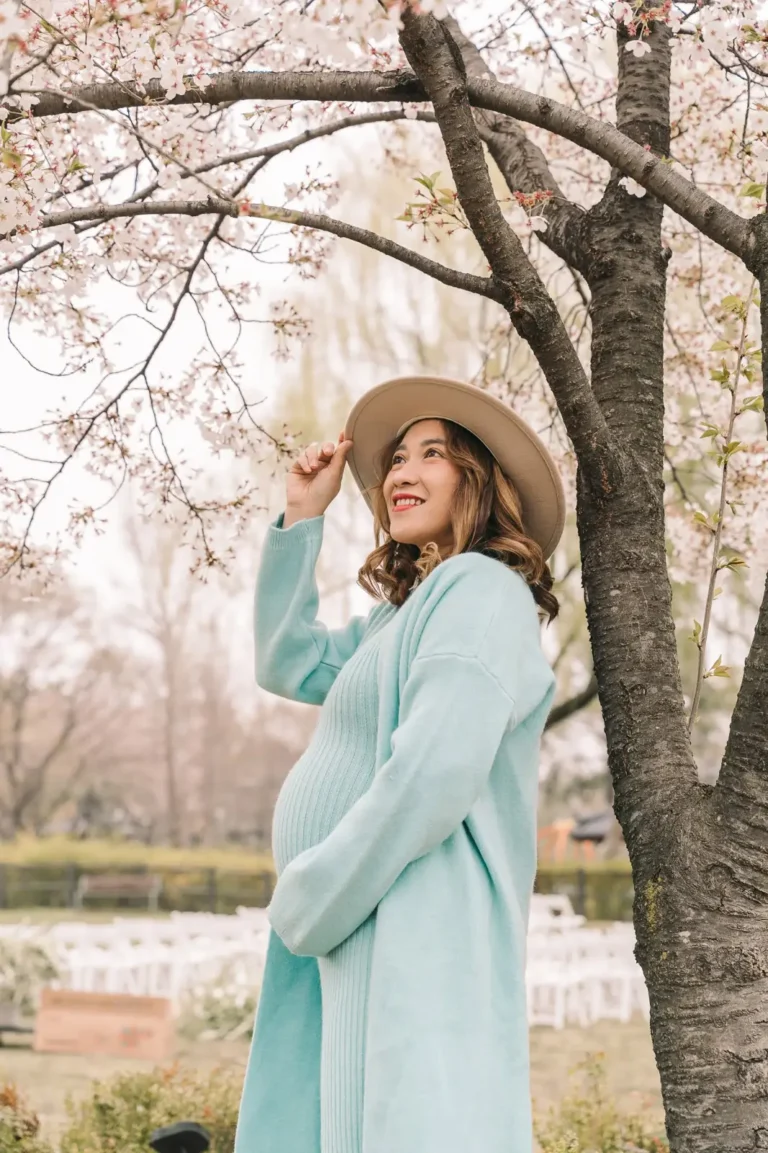 Pregnant woman smiling beneath pink cherry blossoms during a Seoul maternity photoshoot