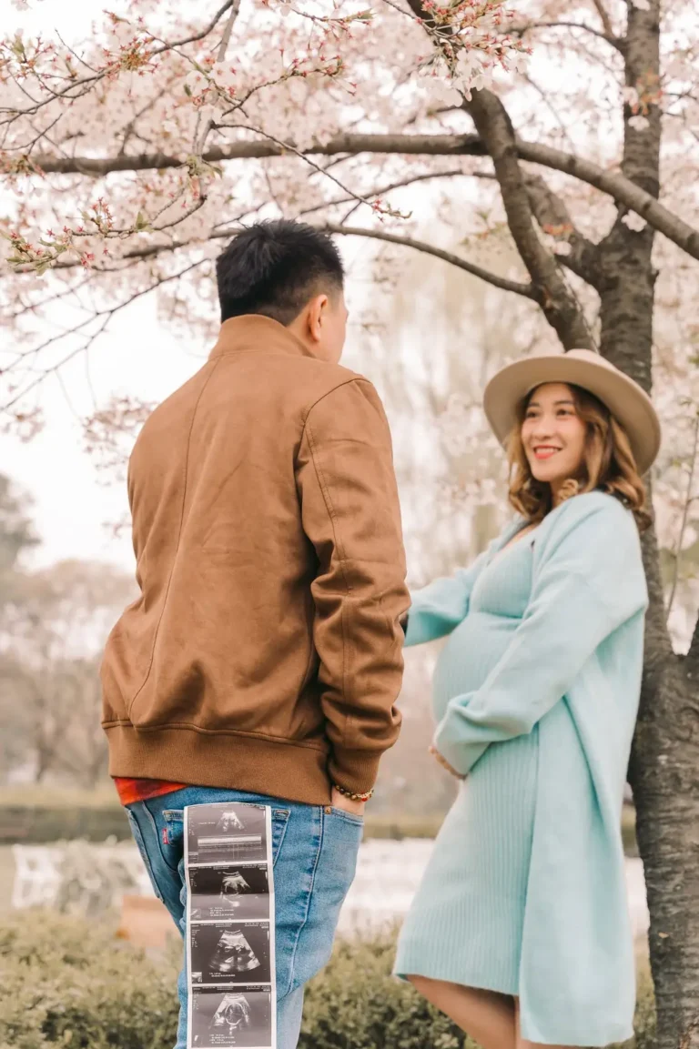 Expecting couple smiling together beneath cherry blossoms during a Seoul maternity session