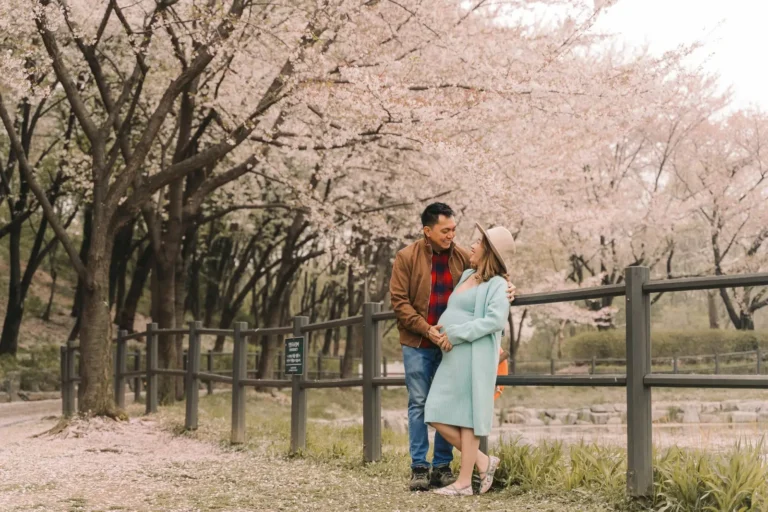 Expecting couple walking hand in hand beneath cherry blossoms in Seoul