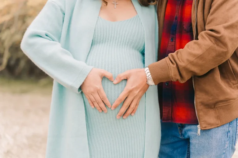 Expecting parents forming a heart with their hands over the pregnant belly