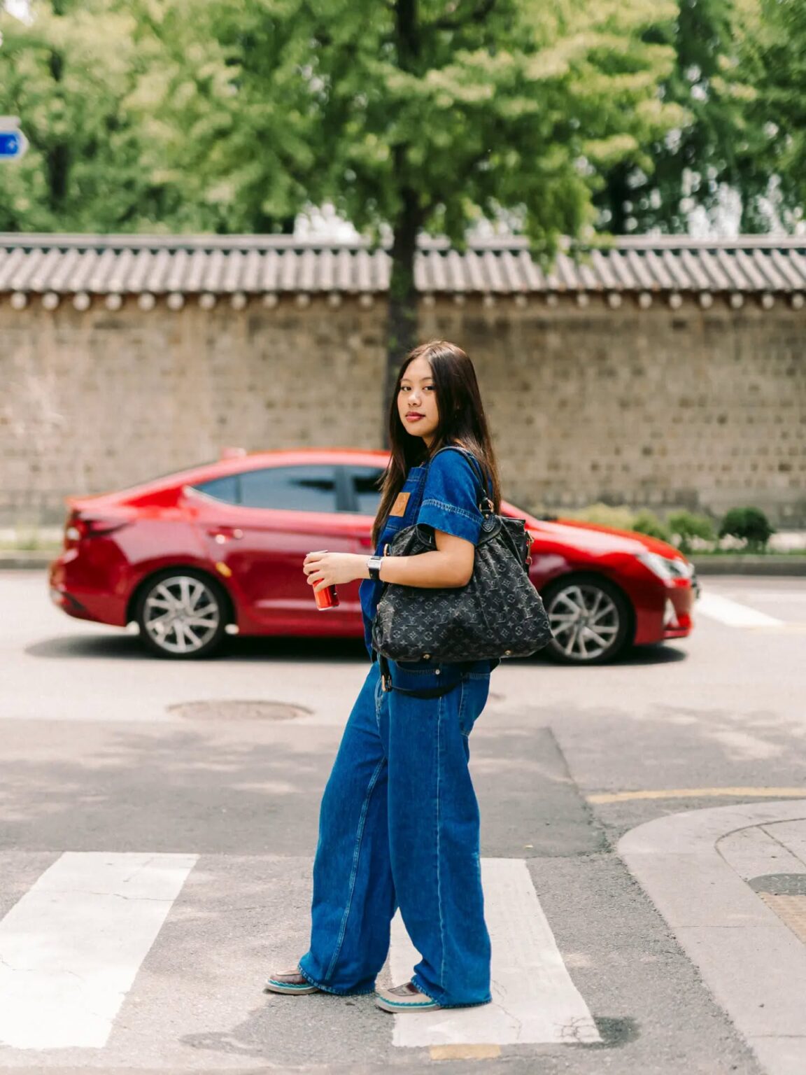 Woman walking along a Seoul street beside a traditional Korean stone wall during a candid portrait photoshoot.
