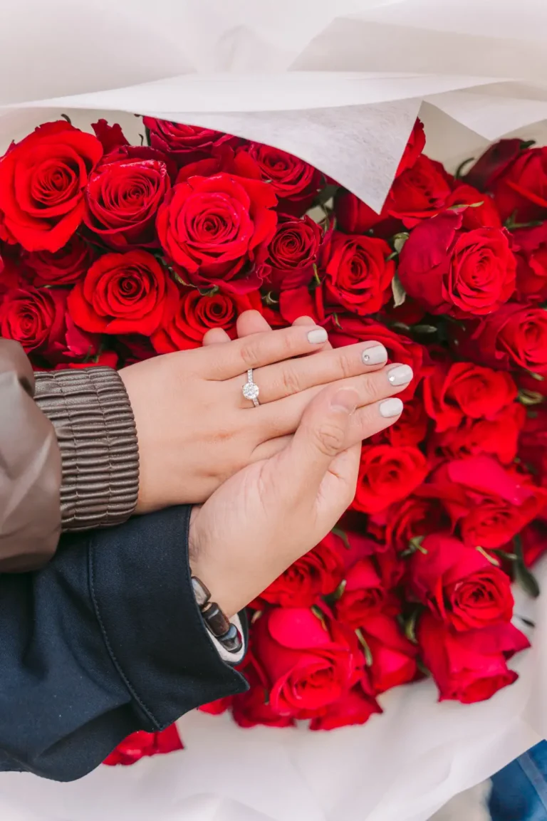 Close-up of an engagement ring against a bouquet of red roses