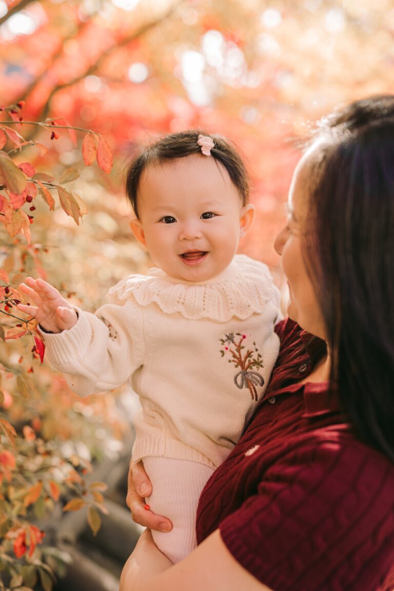 Smiling baby being held beside bright red autumn foliage during a Seoul photoshoot