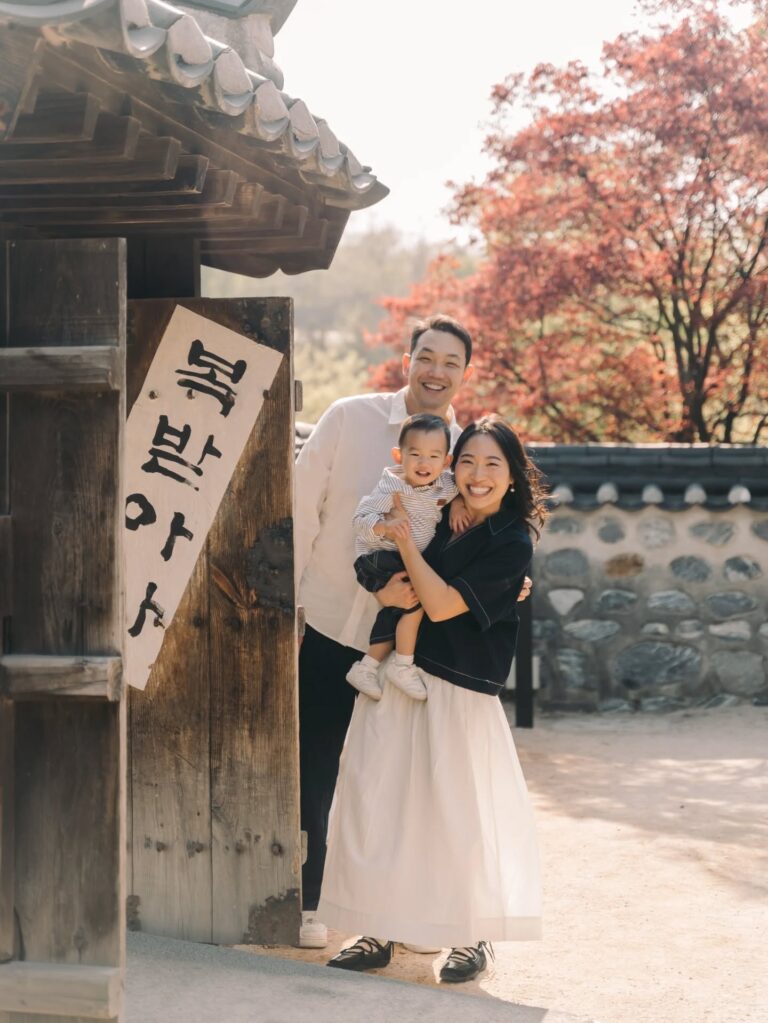 Parents holding their baby together beside traditional architecture and autumn leaves in Seoul
