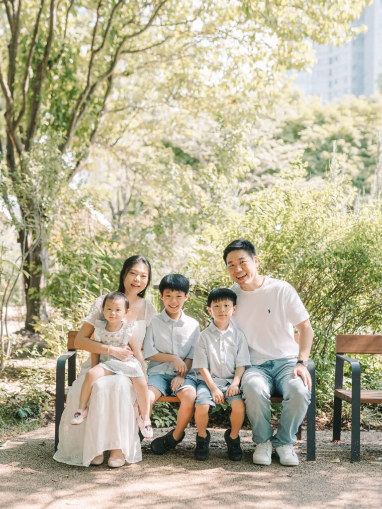 Parents and three children sitting together on a park bench during a Seoul family photoshoot