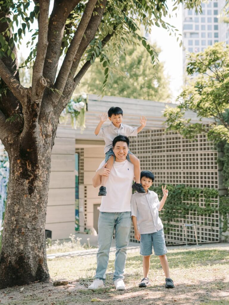 Father carrying one child on his shoulders while walking with another child during a Seoul family session