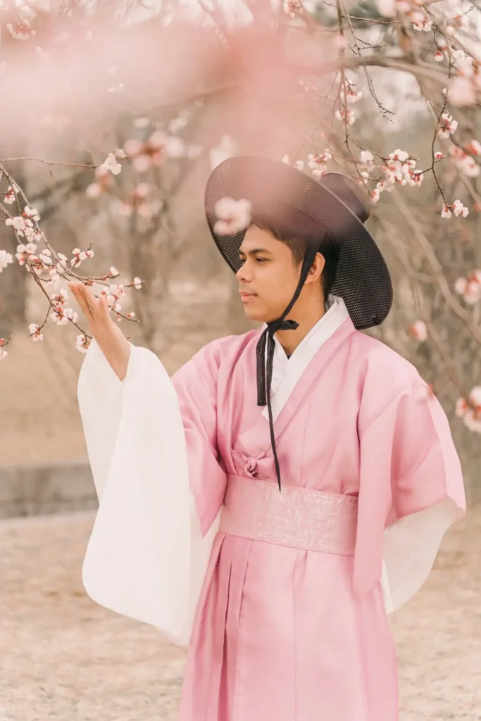 Man wearing pink traditional Korean hanbok beneath spring blossoms in Seoul