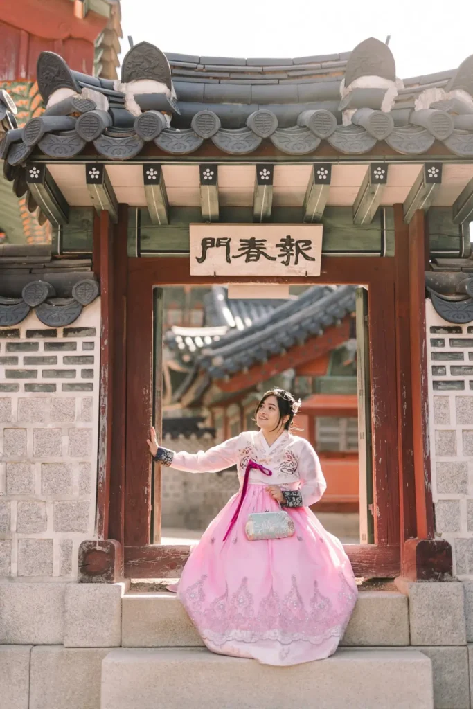 Woman in a pink traditional Korean hanbok posing beneath a historic palace gate