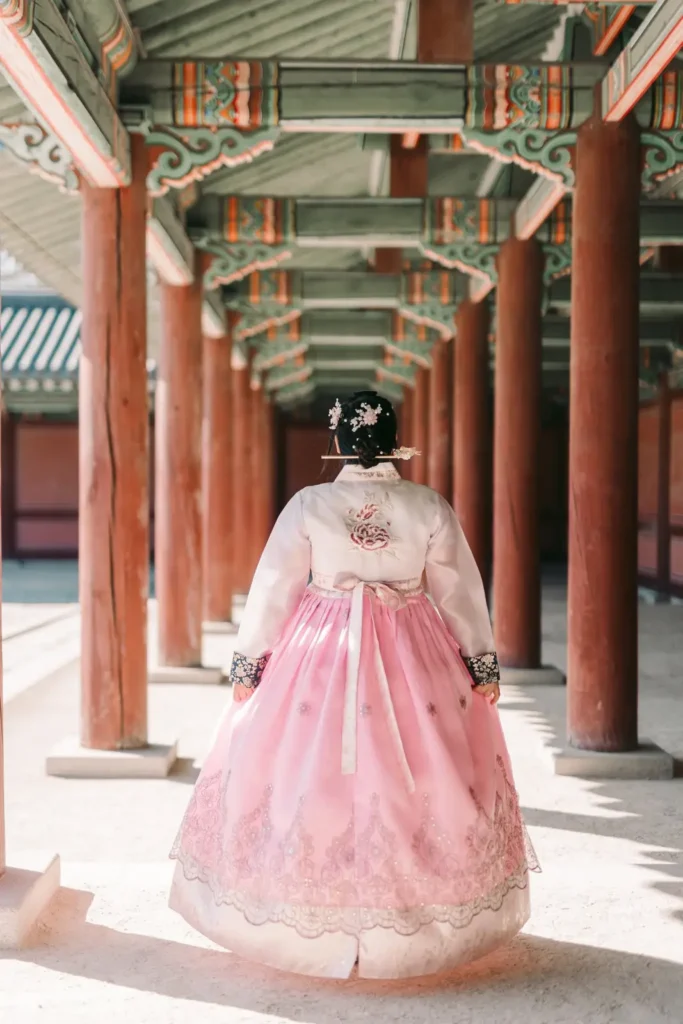 Woman photographed from behind in a pink hanbok beneath Gyeongbokgung Palace columns