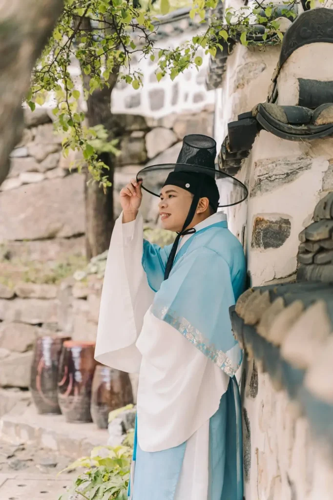Man wearing blue traditional Korean hanbok adjusting his gat during a palace photoshoot