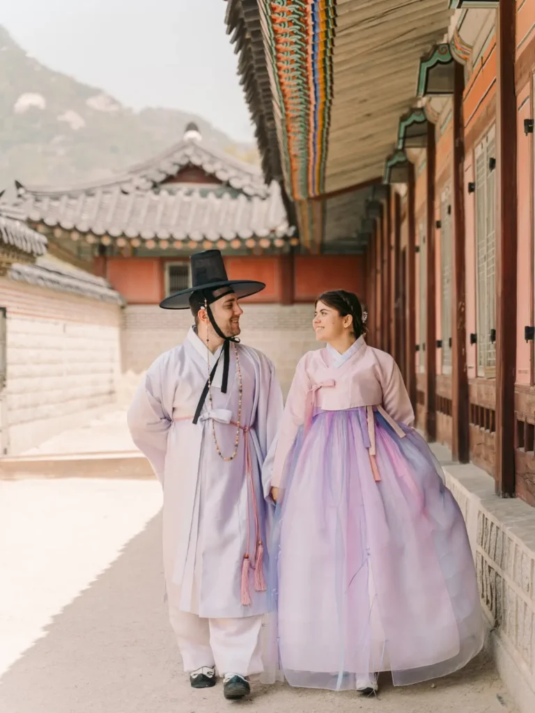 Couple wearing pastel pink and purple hanbok walking through Gyeongbokgung Palace