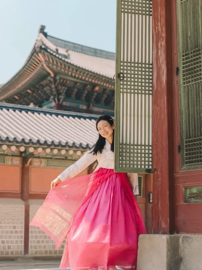 Woman showing her flowing pink hanbok beside traditional palace architecture