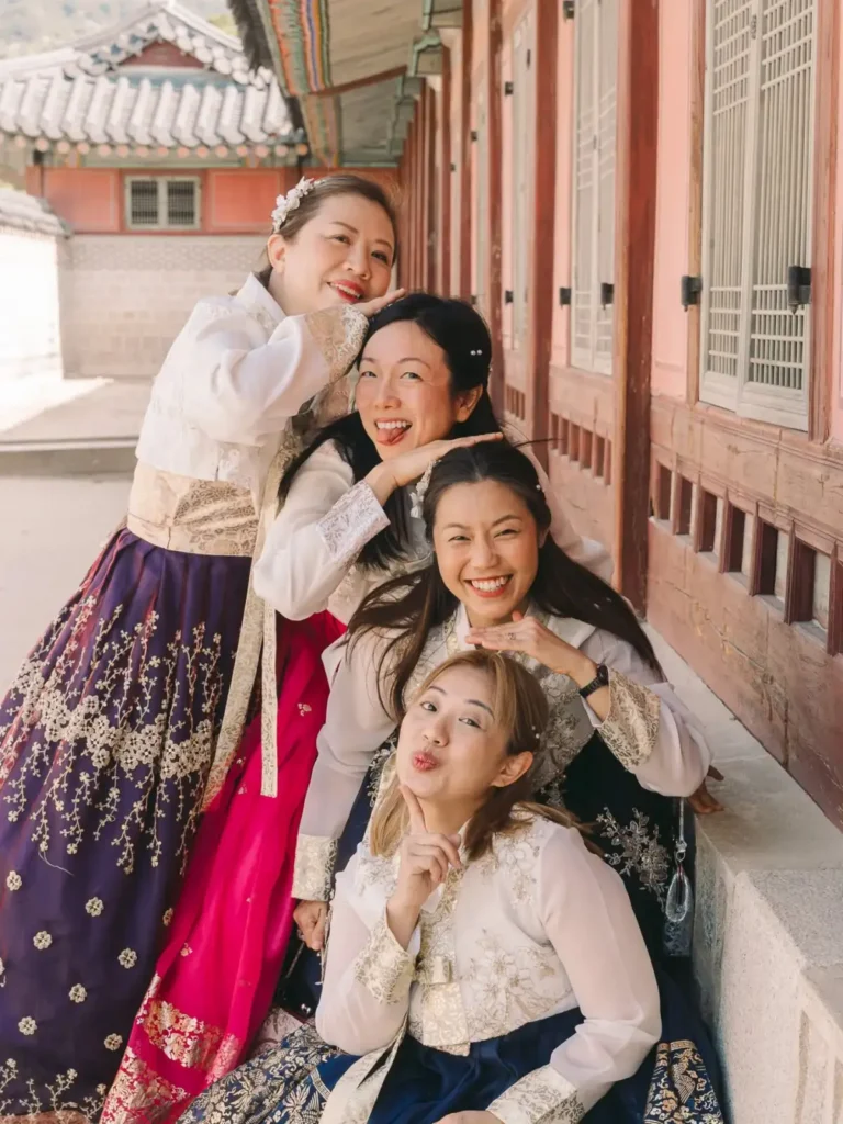 Four women in traditional Korean hanbok laughing together at Gyeongbokgung Palace