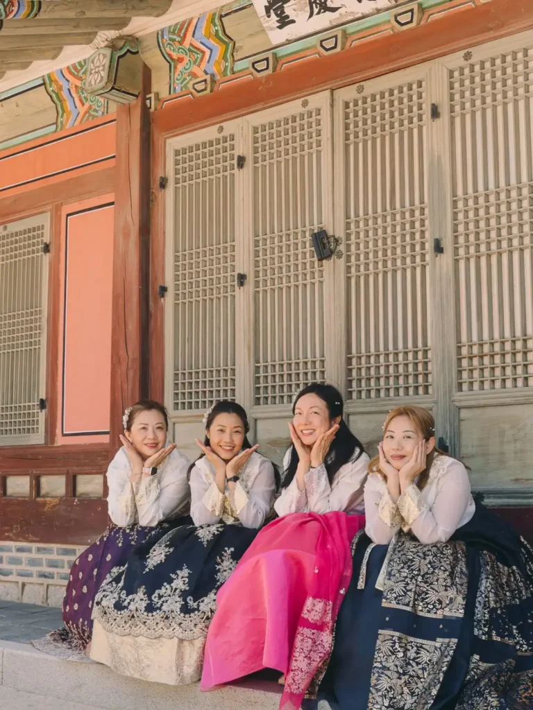 Four friends wearing Korean hanbok posing together outside a palace building