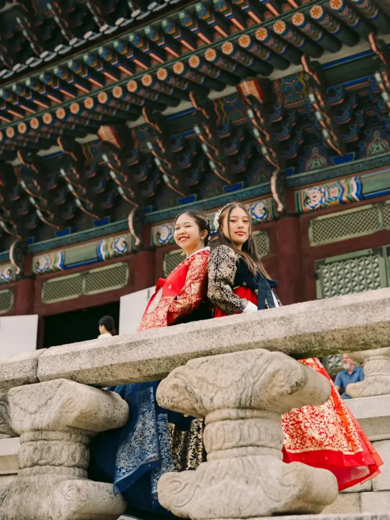 Two women wearing colorful traditional Korean hanbok posing beneath palace architecture