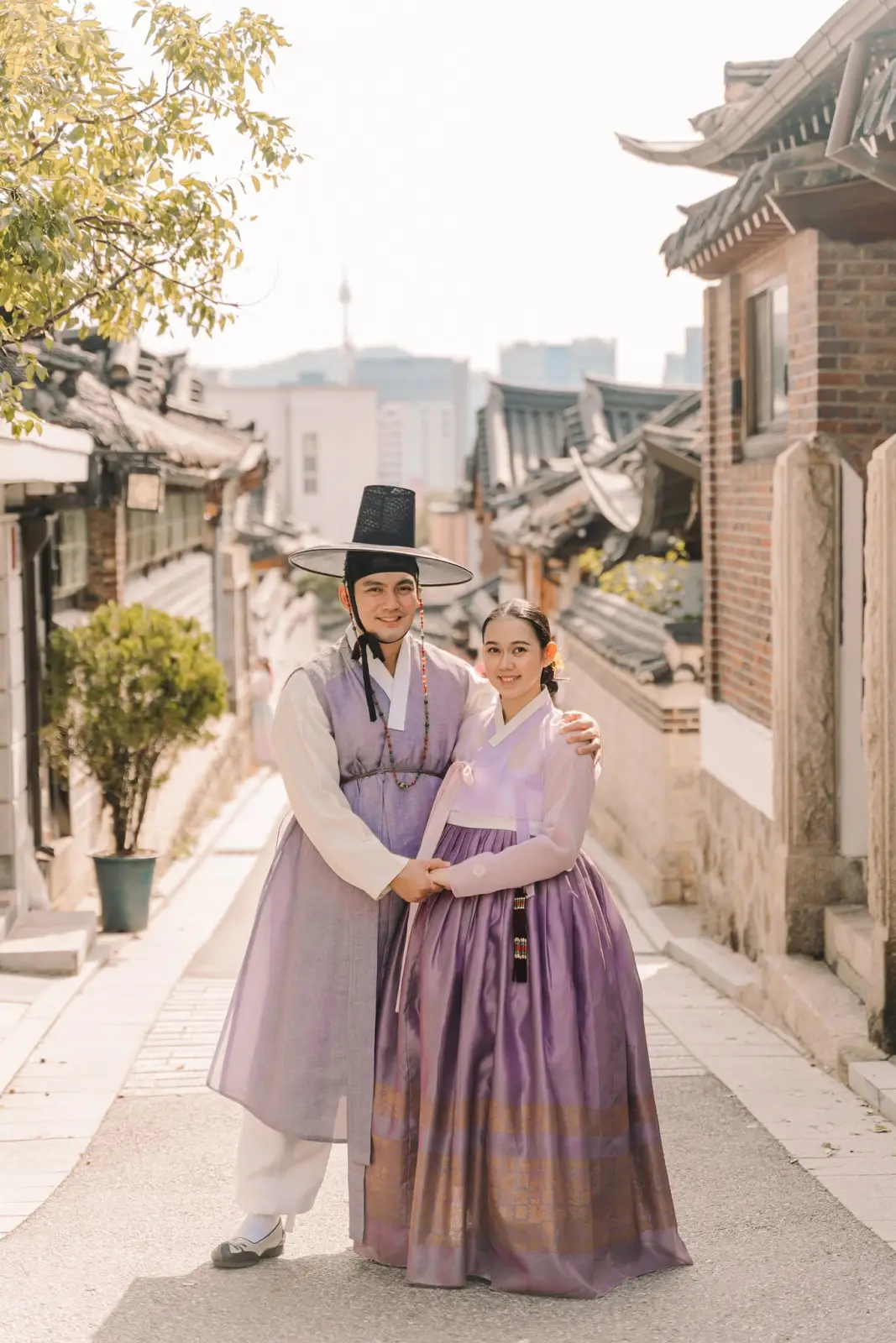 Couple wearing purple traditional Korean hanbok posing along a historic Seoul street